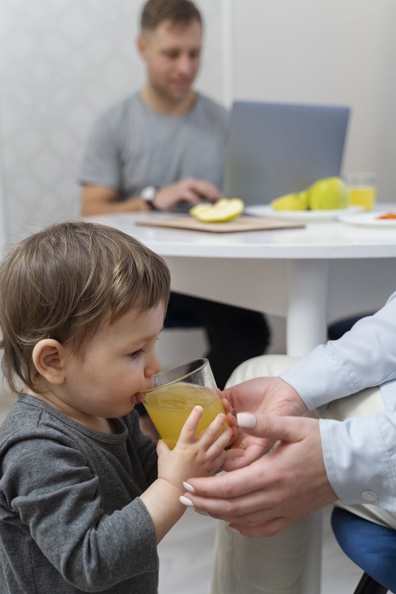 Toddler happily drinking juice from a glass held by a caregiver